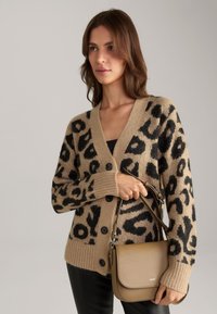 Cardigan beige con stampa leopardata nera, scollo a V e bottoni neri. Abbinato a una borsa color cammello con pattina e tracolla regolabile.