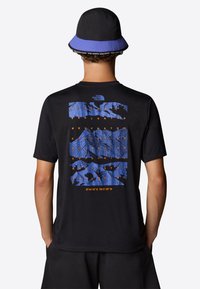 Camiseta negra de manga corta con un gráfico de montaña azul en la parte de atrás, acompañado de texto naranja y coordenadas. Complementada con un sombrero tipo cubo azul y negro.