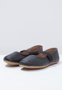 Sorte lær balletlejligheder med rund tå, der har en glitrende rem over vristen og en tan gummi sål.