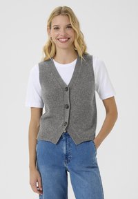Grau gestrickte Weste mit V-Ausschnitt, die vier Vorderknöpfe und einen leicht geschwungenen Saum hat. Über einem weißen T-Shirt und blauen Jeans getragen.