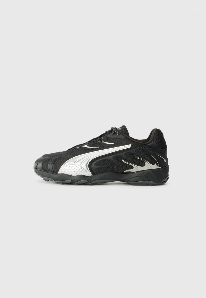 Zapatilla deportiva negra con acentos plateados, parte superior texturizada y suela acolchada. Presenta elementos de diseño curvados y un sistema de cordones.