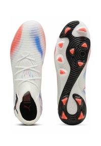 Zapatillas deportivas blancas con acentos de color degradado en rojo y azul; parte superior texturizada, suela negra flexible con distintivos tacos y surcos en naranja.