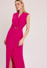 Fuksjowa sukienka bez rękawów z głębokim dekoltem w kształcie V, z wciętą talią ozdobioną złotym okrągłym klamrą oraz bocznym rozcięciem dla dodatkowego efektu.