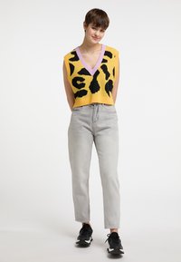 Gul strikket crop top med sorte mønstre og lavendel v-hals, parret med lysegrå tapered jeans og sorte sneakers.