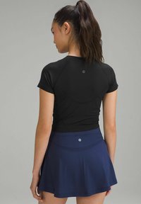 Zwarte fitted T-shirt met korte mouwen, gecombineerd met een marineblauwe rok met een textuurpatroon en logo op de tailleband. Achteraanzicht benadrukt de halslijn en pasvorm.