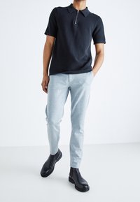 Czarna koszulka polo z krótkim rękawem i zamkiem błyskawicznym przy kołnierzyku, połączona ze jasnoszarymi spodniami w fasonie slim fit oraz czarnymi botkami za kostkę. Gładki materiał i dopasowany krój.