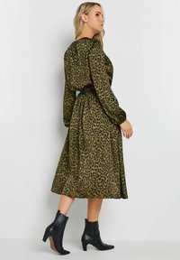 Vestido verde con estampado de leopardo, de manga larga, con la cintura ajustada y una falda que fluye. Combinado con botas negras hasta el tobillo. Textura suave.