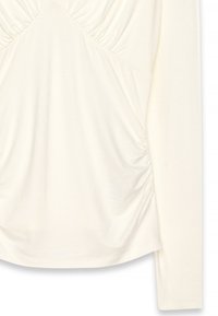 Dolgimi rokavi v kremni tkanini z nabranimi detajli na prsi in straneh, gladka tekstura ter okroglen rob.
