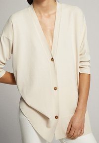 Beige Strickjacke mit tiefem V-Ausschnitt und übergroßer Passform, mit vier Holzknöpfen und gerippten Bündchen an den Ärmeln.
