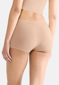 Beige sömlösa boxershorts gjorda av ett mjukt tyg, med en bekväm passform och ett elastiskt midjeband samt minimala sömnadsdetaljer.