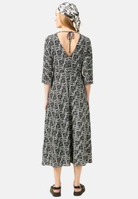 Schwarz-weiß gemustertes Kleid mit Dreiviertelärmeln, tiefem V-Ausschnitt im Rücken und einer Bindeschließe. Kombination mit einem passenden Schal und Sandalen.