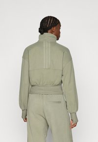 Ανοιχτό πράσινο φούτερ με ψηλό γιακά, ριγμένες μανσέτες και λάστιχο στη μέση. Διαθέτει κάθετες ραφές στην πλάτη και χαλαρή γραμμή.