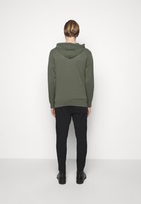 Bluza z kapturem w oliwkowym kolorze, uszyta z miękkiego materiału, z prążkowanymi mankietami i dołem. W połączeniu z czarnymi tapered joggerami i czarnymi butami.