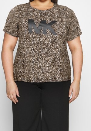 Osoba plus size ubrana w brązową koszulkę z krótkim rękawem w panterkę z dużymi czarnymi literami "MK" oraz czarne spodnie na białym tle.