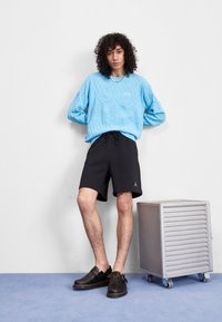 Light blue textured sweater, black shorts with drawstring, black slip-on shoes. Silver metal container on blue carpet.