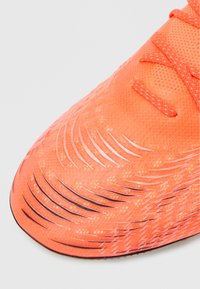 Kirkkaan oranssi jalkapallokenkä, jossa on teksturoitu päällinen, kontrastiväriset mustat raidat ja keskitetysti sijoitetut nauhat. Suunniteltu ketteryyttä ja pitoa varten.