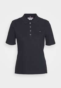 Polo shirt noir à manches courtes avec quatre boutons, col, et petit logo rouge, blanc et bleu de Tommy Hilfiger sur la poitrine gauche.