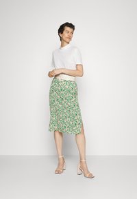 T-shirt branco de mangas curtas, combinado com uma saia midi floral verde, com flores rosas e brancas. Usado com sandálias de salto bege.
