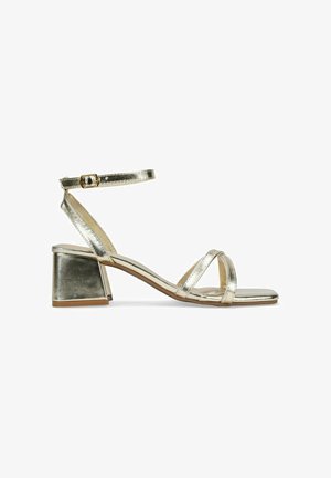 Metallic gold heeled sandals with a square block heel, slim ankle strap, and crisscrossed front bands. Smooth texture and minimal design.