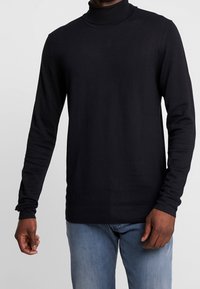 Schwarzer Rollkragenpullover aus geripptem Strickgewebe mit langen Ärmeln, in taillierter Form und glatter Textur, kombiniert mit hellblauen Jeans.