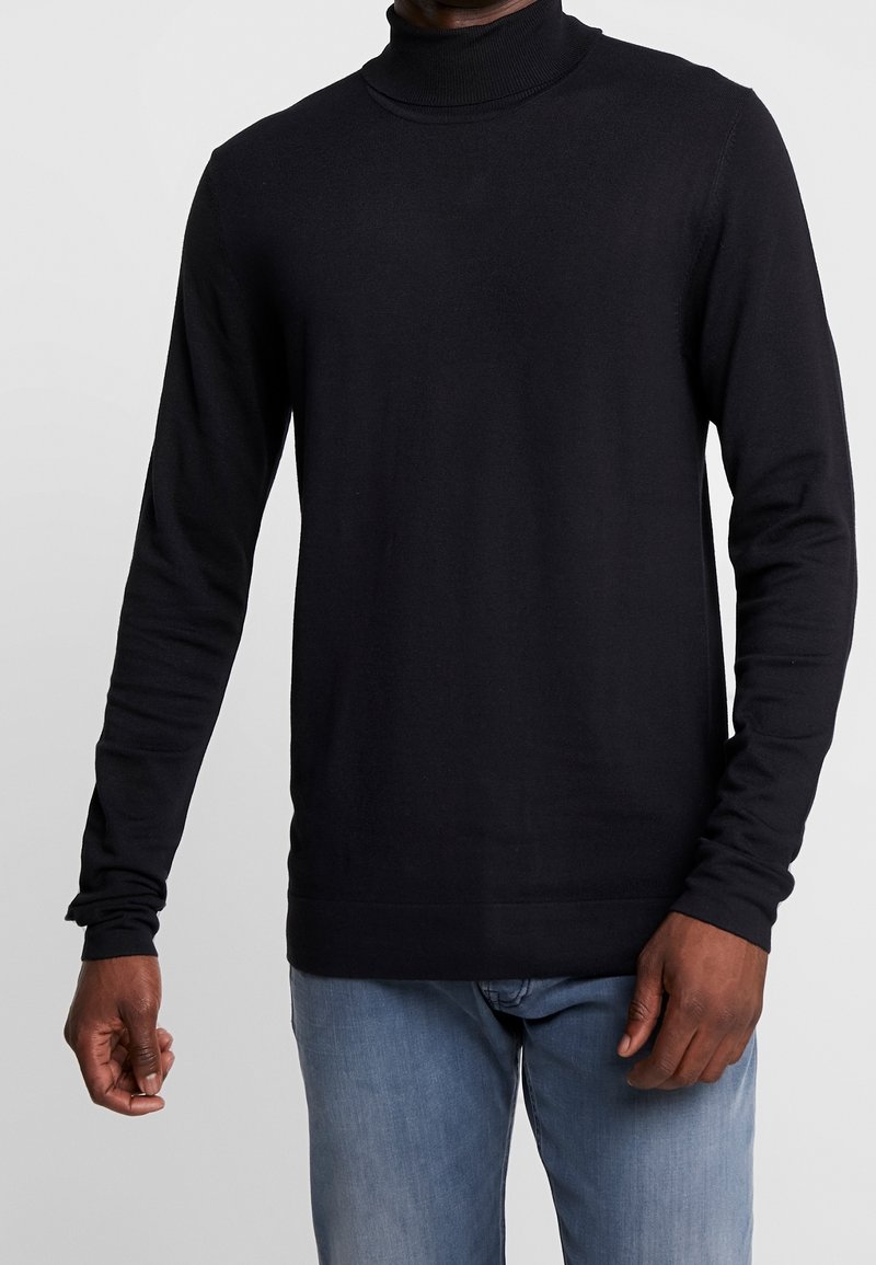 Schwarzer Rollkragenpullover aus geripptem Strickgewebe mit langen Ärmeln, in taillierter Form und glatter Textur, kombiniert mit hellblauen Jeans.
