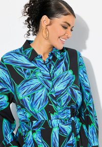 Blå och grön blommönstrad skjorta med svart bakgrund, med krage, knäppning och bälte i midjan.