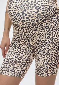 Κοντινή λήψη προσώπου που φοράει εφαρμοστά σορτς με μοτίβο λεοπάρ σε μπεζ και μαύρο, με αντίθετη ραφή και ορατά τατουάζ στον αριστερό πήχη.