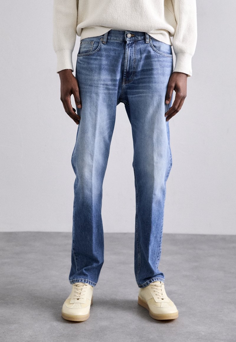 Ljusblå denimjeans med rak passform, blekt tvätt, femfickdesign och silvrig knappknäppning. I kombination med krämfärgade sneakers.