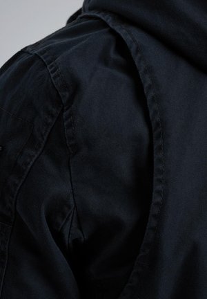 Gros plan sur un tissu bleu marine présentant une chemise à col avec une texture lisse et des coutures visibles au niveau de l'épaule et du col.