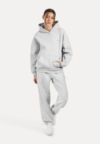 Felpa grigia in cotone con tasca frontale e pantaloni coordinati. Il tessuto ha una consistenza morbida, con polsini elasticizzati sui pantaloni.