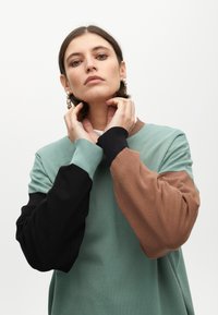 Mikina s kulatým výstřihem, vyrobená z měkké tkaniny, s rukávy v mintově zelené, hnědé a černé barvě. Žebrované manžety a lem.