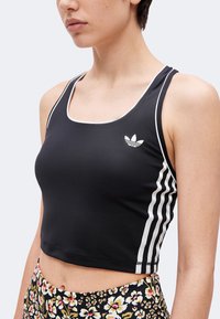 Γυναίκα που φοράει μαύρο crop top με λευκή επένδυση και τρεις λευκές ρίγες στο πλάι, σε συνδυασμό με παντελόνι με λουλουδάτο μοτίβο.