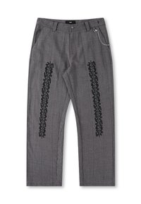 Pantalon à carreaux gris avec texte graphique noir vertical sur les jambes et une petite chaîne argentée attachée près de la poche droite.