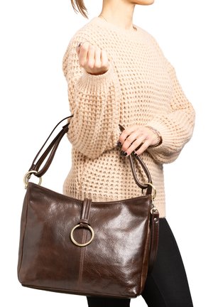 Borsa a mano in pelle marrone con una texture liscia, caratterizzata da un'acceleratore metallica circolare e doppie spalline, tenuta da una persona che indossa un maglione di lana.