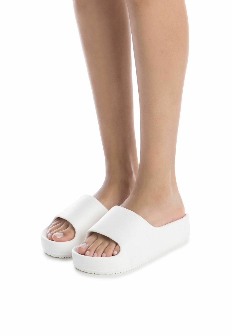Sandalias de plataforma blancas con una correa ancha y punta abierta, que cuentan con una superficie texturizada y una suela gruesa. Diseño ligero y casual.