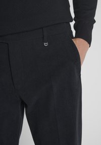 Donker corduroy broek met een op maat gemaakte pasvorm, vlakke voorkant en zijzakken, met een subtiele metalen accent op de tailleband.