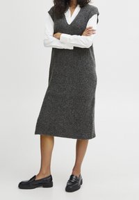 Robe gris côtelée en maille avec un col en V et sans manches, atteignant le milieu du mollet. Associée à des mocassins noirs pour un look monochrome.