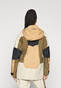 Farbblockierte Jacke mit beigen, braunen und marineblauen Panels. Hergestellt aus strukturiertem Stoff, verfügt sie über eine Kapuze und verstellbare Manschetten.