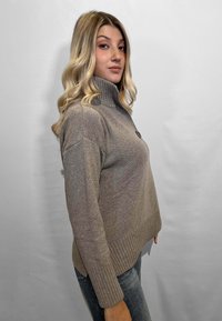 Maglione taupe chiaro con colletto alto, polsini e orlo a coste. Texture liscia con un dettaglio di un solo bottone sul davanti.