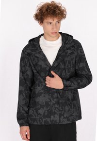Giacca nera a motivo, realizzata in materiale impermeabile, con zip, cappuccio regolabile e tasche frontali con design esagonale.