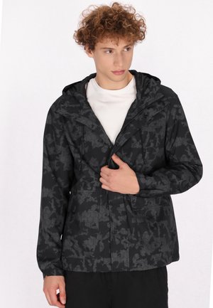 Jachetă neagră cu model, fabricată din material rezistent la apă, având fermoar, glugă ajustabilă și buzunare frontale cu un design hexagonal.