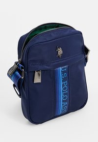 Laivastonsininen nylonista valmistettu olkalaukku, jossa on etutasku vetoketjulla, U.S. Polo Assn. -brändäys sinisenä, hopeanväriset metalliosat ja vihreä vuori.