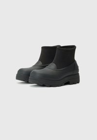 Bottes de cheville noires imperméables avec une tige en caoutchouc lisse, une manche élastique texturée et une semelle extérieure épaisse et robuste pour une meilleure adhérence.