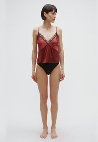 Sarkana satīna krekliņa ar melnām mežģīnēm malā, ar plāniem siksniņām un ērtu piegriezumu, kopā ar melniem augsta vidukļa biksītēm.