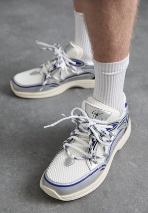 Sneakers bianche con dettagli blu e argentati. Materiale in mesh, lacci distintivi, collo imbottito, suola spessa in gomma. Calzini bianchi a coste.