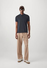 Marinblå pikétröja, beige vidbyxade byxor, brun keps, svarta solglasögon, vita skor med bruna detaljer, minimalistisk design, slät textur.