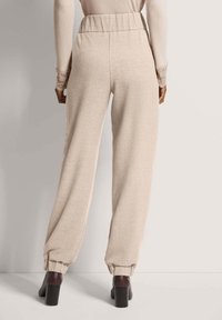 Beige, lockere Hose mit elastischem Bund und schmal zulaufenden Bündchen. Glattes, strukturiertes Gewebe. Kombiniert mit dunklen Absatzschuhen.