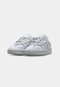 White leather sneakers with grey rubber soles, featuring three grey stripes on each side, round toes, and silver shoelaces.
