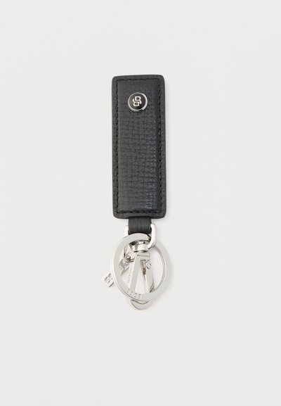 Porte-clés en cuir noir texturé avec anneaux et clips métalliques argentés, orné d'un petit bouton rond avec logo sur la lanière en cuir.