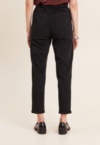 Schwarze Baumwollhose mit elastischem Bund, ausgestattet mit zwei Gesäßtaschen und umgeschlagenen Säumen. Sie hat eine gerade Beinform und eine glatte Textur.